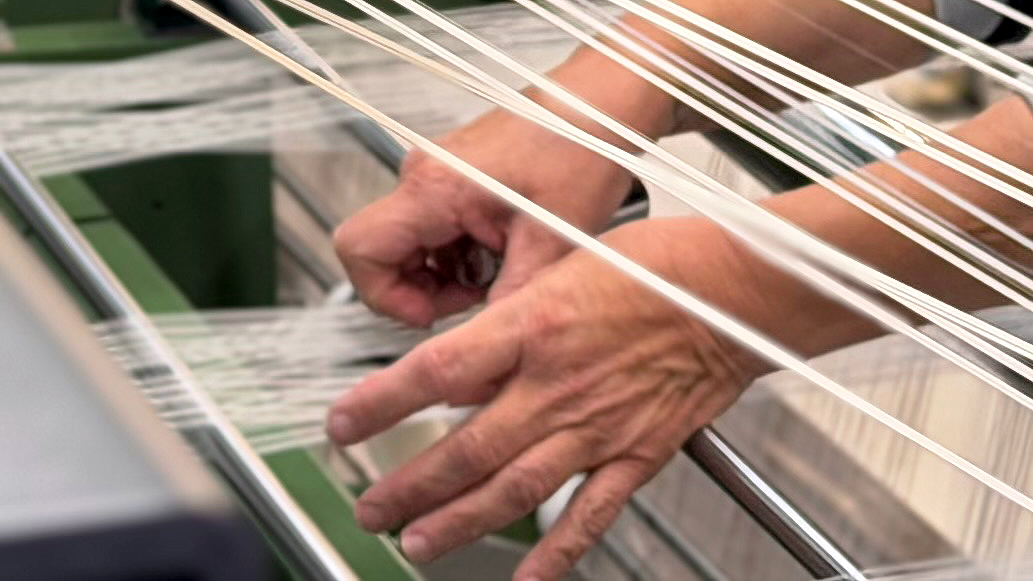 Close-up of a worker's hands guiding fibers through textile weaving equipment at ATEX.