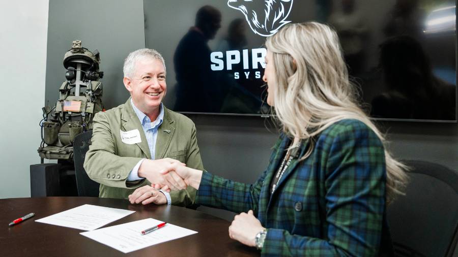 Two professionals shake hands during a signing event at Spiritus Systems.