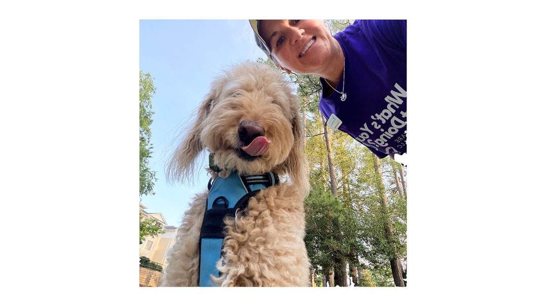 PetWise Professionals owner Anna Vermeulen poses outdoors with a dog wearing a blue harness.