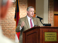 Sandhills Community College President Alexander “Sandy” Stewart speaks at a podium during a graduation ceremony.