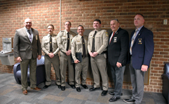 Basic Law Enforcement Training graduates in khaki uniforms pose with local law enforcement leaders, including Sheriff Ronnie Fields, Major Eric Galloway, and Chief Deputy Andy Conway, at a Sandhills Community College ceremony.