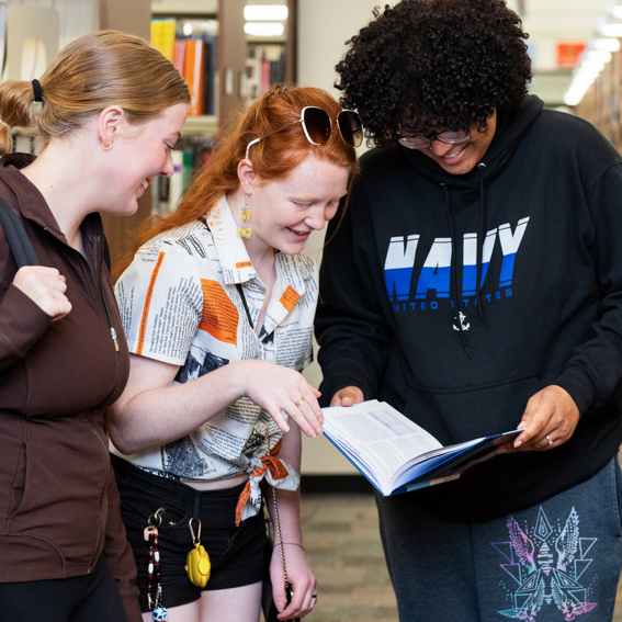 Four Sandhills Community College students review a book together in the campus library aisle.