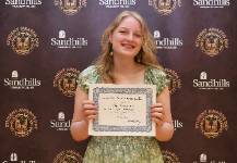 Student Abigail Kirkham holding an award certificate and smiling in front of a Sandhills Community College Student Awards Day backdrop.