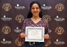 Student Danely Maldanado holding an award certificate and smiling in front of a Sandhills Community College Student Awards Day backdrop.