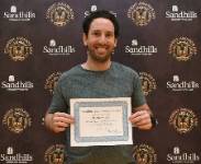 Student Matthew Celia holding an award certificate and smiling in front of a Sandhills Community College Student Awards Day backdrop.