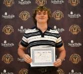 Student Ryan Watson holding an award certificate and smiling in front of a Sandhills Community College Student Awards Day backdrop.