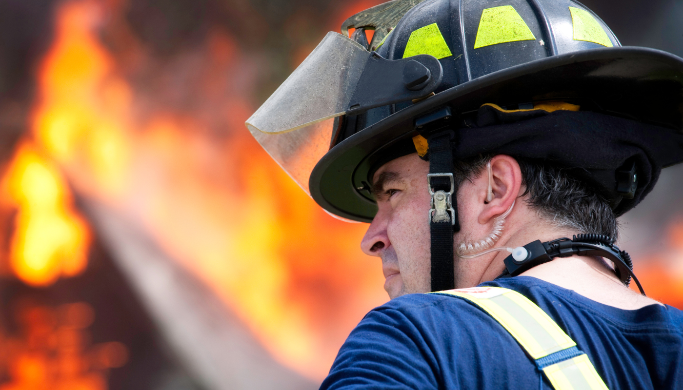 The profile of a firefighter standing outside a blaze. 