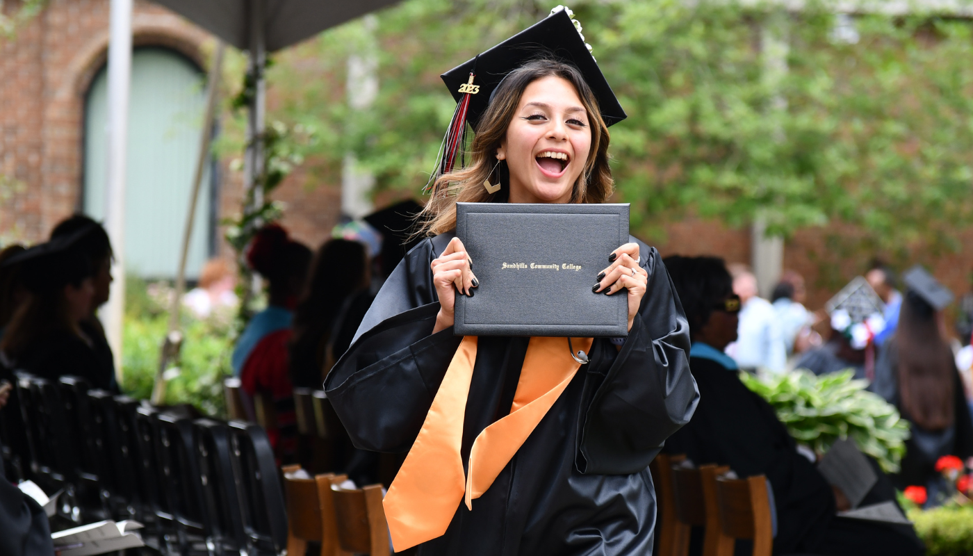 Pictured is a student smiling and holding her diploma after she just walked across the stage. 