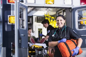 Paramedic smiling in front of ambulance with open doors.