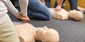 A group of adult education students practicing CPR chest compression on a mannequin.