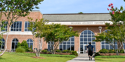 View of Dempsey Student Center on a sunny day, a student walking in front.