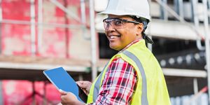 Person smiling, at a construction site, holding an iPad.