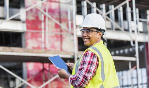Person smiling, at a construction site, holding an iPad.