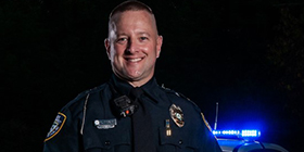 SCC graduate Steve Engle poses at night, in police uniform, in front of his police car.