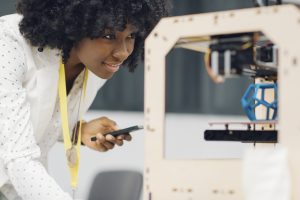 Person looking at a 3D printer, with an object being printed.